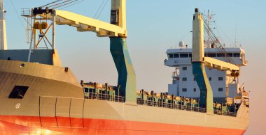 Büyük vinç gemisi (genel yük, 146 metre uzunluğunda) gün batımında açık denizde yol alır. Altın güneş ışığı. Yük taşımacılığı, lojistik, küresel iletişim, ekonomi, sanayi, dünya çapında taşımacılık