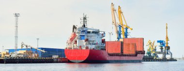 Liman terminalinde büyük bir kargo gemisi yükleniyor, arka planda vinçler var. Yük taşımacılığı, lojistik, küresel iletişim, ekonomi, ticaret, sanayi, özel ekipman