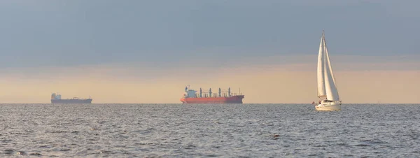 スループはバルト海を航行するヨットを操縦した 嵐の後に劇的な空 黄金の太陽 背景に貨物船 クルーズ ヨットレース スポーツ レクリエーション — ストック写真