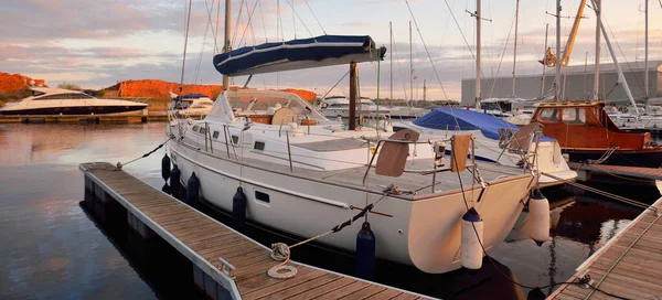 Günbatımında yat limanındaki bir rıhtıma demirlenmiş ahşap meşe güverteli modern yelkenli. Dramatik gökyüzü, parlayan altın bulutlar. Tatiller, ulaşım, spor, eğlence, turizm, seyahat, liman