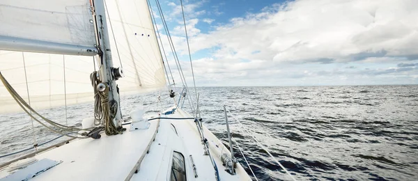 White sloop rigged yacht sailing in an open sea on a clear day. A view from the deck to the bow. Cumulus clouds. Transportation, travel, cruise, sport, recreation, leisure activity, racing, regatta