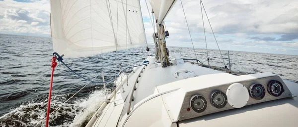 Açık bir günde açık denizde yelken açan beyaz yelkenli bir yat. Güverteden pruvaya bir manzara. Kümülüs bulutları. Ulaşım, seyahat, gezi, spor, eğlence, boş zaman aktivitesi, yarış, yelkenli yarışı