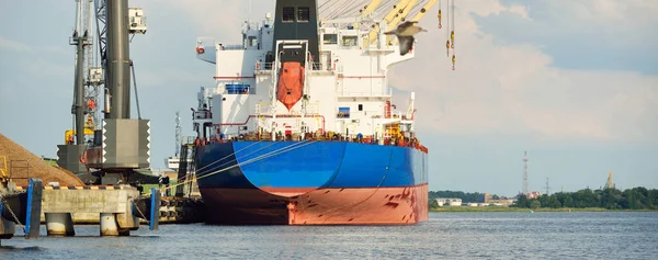 Liman terminalinde büyük bir kargo gemisi yükleniyor, arka planda vinçler var. Yük taşımacılığı, deniz taşımacılığı, lojistik, küresel iletişim, dünya çapında taşımacılık, ekonomi, ticaret, sanayi