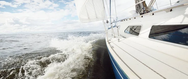 Açık bir günde açık denizde yelken açan beyaz yelkenli bir yat. Güverteden pruvaya bir manzara. Kümülüs bulutları. Ulaşım, seyahat, gezi, spor, eğlence, boş zaman aktivitesi, yarış, yelkenli yarışı