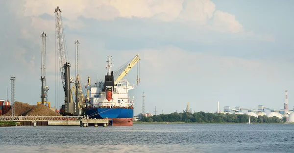 Liman terminalinde büyük bir kargo gemisi yükleniyor, arka planda vinçler var. Yük taşımacılığı, deniz taşımacılığı, lojistik, küresel iletişim, dünya çapında taşımacılık, ekonomi, ticaret, sanayi