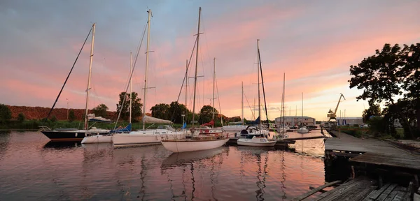 Günbatımında yat limanında demirlemiş zarif ve modern yelkenliler. Dramatik gökyüzü, parlayan altın bulutlar. Tatiller, ulaşım, spor, eğlence, turizm, seyahat, liman