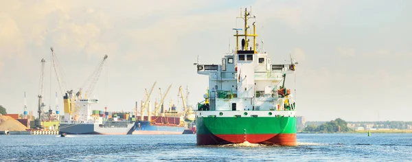 日没時に貨物ターミナルに到着する大規模な緑のばら積み貨物船 背景にある船やクレーン 劇的な雲景 貨物輸送 グローバル通信 — ストック写真
