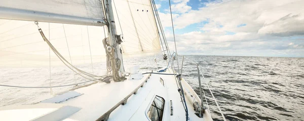Açık bir günde açık denizde yelken açan beyaz yelkenli bir yat. Güverteden pruvaya bir manzara. Kümülüs bulutları. Ulaşım, seyahat, gezi, spor, eğlence, boş zaman aktivitesi, yarış, yelkenli yarışı