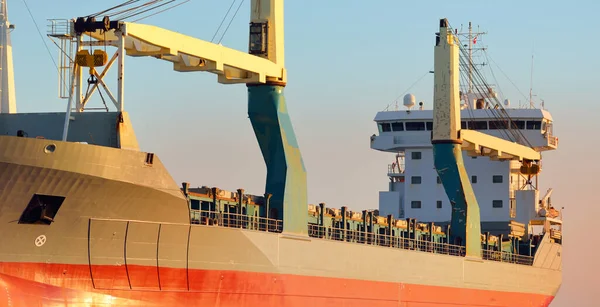 Büyük vinç gemisi (genel yük, 146 metre uzunluğunda) gün batımında açık denizde yol alır. Altın güneş ışığı. Yük taşımacılığı, lojistik, küresel iletişim, ekonomi, sanayi, dünya çapında taşımacılık
