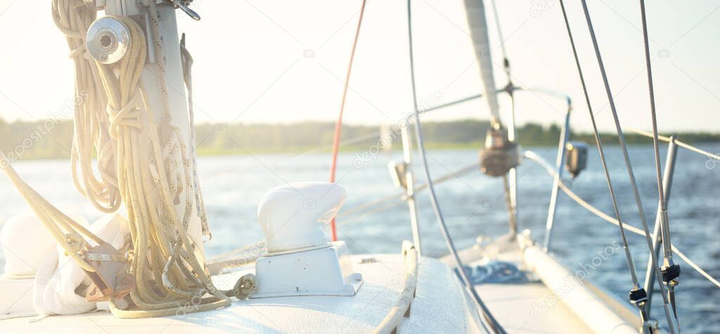White sloop rigged yacht sailing on a clear day. A view from the deck to the mast and bow. Rigging equipment, ropes close-up. Transportation, travel, cruise, recreation, leisure activity, regatta