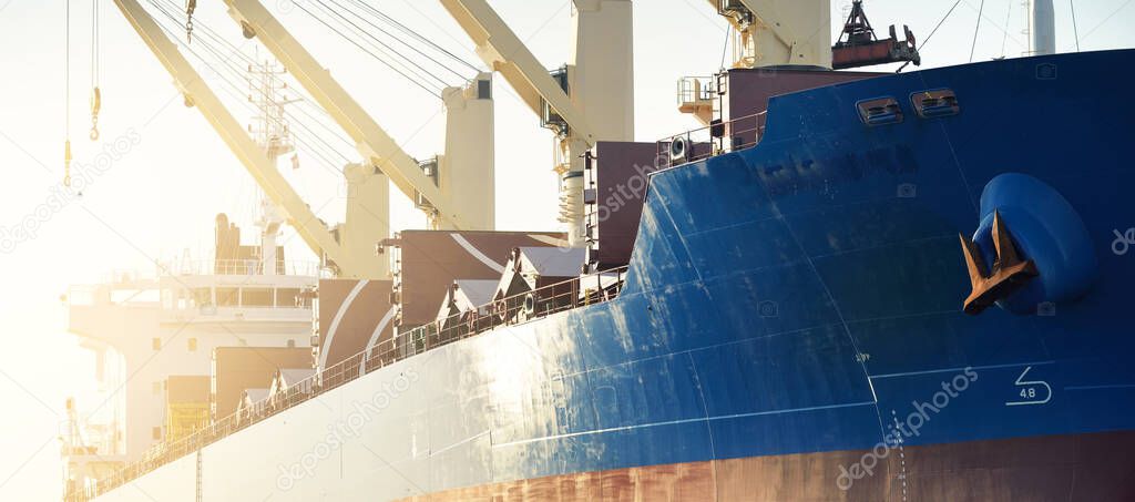 Large cargo ship loading in port terminal, cranes in the background. Freight transportation, nautical vessel, logistics, global communications, worldwide shipping, economy, business, industry