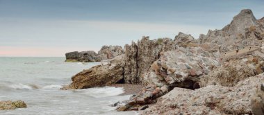Gün batımında Baltık kıyılarından (plaj) panoramik manzara. Harabeler ve kayalar. Resimli bir manzara var. Dramatik bir gökyüzü. Doğa, seyahat yerleri, dönüm noktaları, yaz tatilleri, turizm, tarih kavramları