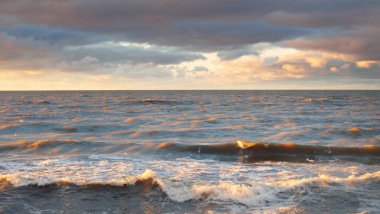 Gün batımında Baltık kıyısı. Yumuşak altın güneş ışığı, dramatik gökyüzü, parlayan bulutlar, dalgalar. Idyllic deniz manzarası. Seyahat yerleri, eko-turizm, doğa, hava durumu, iklim değişikliği. Resimli panoramik manzara