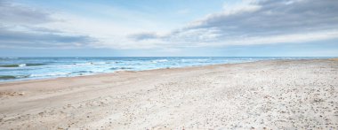 Kumlu bir sahilden (kum tepeleri) Baltık denizinin panoramik görüntüsü. Parlayan bulutlar, dalgalar ve su sıçramalarıyla dramatik bir gökyüzü. Idyllic deniz manzarası. Sıcak kış havası, iklim değişikliği, doğa. Danimarka