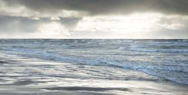 Kumlu bir sahilden (kum tepeleri) Baltık denizinin panoramik görüntüsü. Koyu bulutlu dramatik bir gökyüzü. Dalgalar, su sıçramaları. Idyllic deniz manzarası. Sıcak kış havası, iklim değişikliği, doğa. Danimarka