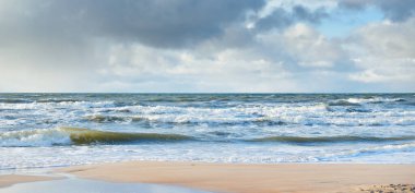 Kumlu sahilden Baltık denizinin panoramik görüntüsü (kum tepeleri). Parlayan bulutları, güneş ışınları olan dramatik bir gökyüzü. Dalgalar, su sıçramaları. Idyllic deniz manzarası. Sıcak kış havası, iklim değişikliği, doğa. Danimarka