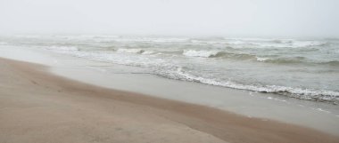 Kalın beyaz bir sis içinde Baltık Denizi. Dalgalar, su sıçratma, fırtına. Doğal dokular. Resimli panoramik monokrom manzarası, deniz manzarası. Doğa, çevre, sert hava, gemi enkazı, tehlike