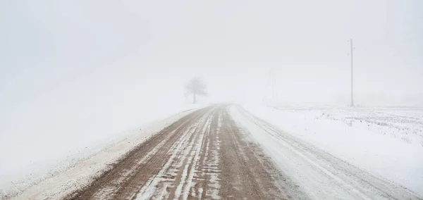 暴风雪期间 乡间小路穿过白雪覆盖的田野 浓密的白雾 孤独的树在后面 大气冬季景观 — 图库照片