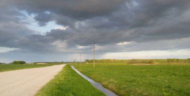 Fırtınadan sonra tarladan geçen boş köy yolu. Arabadan bir manzara. Idyllic kırsal kesim. Renkli, parlayan günbatımı bulutları. Ulaşım, yolculuk, özgürlük, seyahat tutkusu, uzak yerler kavramları.
