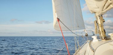 Gün batımında açık denizde yelkenli yelkenli yelkenli. Gökyüzü açık. Güverteden pruvaya bir manzara, direk, yelkenler. Ulaşım, seyahat, gezi, spor, eğlence, boş zaman aktivitesi, yarış, yelkenli yarışı