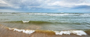 Kumlu bir sahilden (kum tepeleri) Baltık denizinin panoramik görüntüsü. Parlayan bulutlar, dalgalar ve su sıçramalarıyla dramatik bir gökyüzü. Idyllic deniz manzarası. Sıcak kış havası, iklim değişikliği, doğa. Danimarka