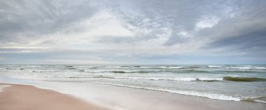 Kumlu bir sahilden (kum tepeleri) Baltık denizinin panoramik görüntüsü. Parlayan bulutlar, dalgalar ve su sıçramalarıyla dramatik bir gökyüzü. Idyllic deniz manzarası. Sıcak kış havası, iklim değişikliği, doğa. Danimarka