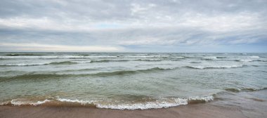 Kumlu bir sahilden (kum tepeleri) Baltık denizinin panoramik görüntüsü. Parlayan bulutlar, dalgalar ve su sıçramalarıyla dramatik bir gökyüzü. Idyllic deniz manzarası. Sıcak kış havası, iklim değişikliği, doğa. Danimarka