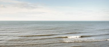 Karla kaplı kumlu sahilden Baltık Denizi 'nin panoramik hava manzarası. Açık gökyüzü, parlayan bulutlar, dalgalar ve su sıçramaları. Deniz Burnu. Sıcak kış havası, iklim değişikliği, doğa. Jurkalne, Letonya