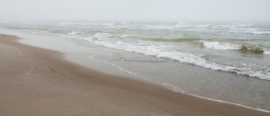 Kalın beyaz bir sis içinde Baltık Denizi. Dalgalar, su sıçratma, fırtına. Doğal dokular. Resimli panoramik monokrom manzarası, deniz manzarası. Doğa, çevre, sert hava, gemi enkazı, tehlike