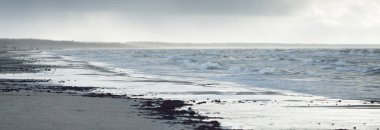 Kumlu bir sahilden (kum tepeleri) Baltık denizinin panoramik görüntüsü. Koyu bulutlu dramatik bir gökyüzü. Dalgalar, su sıçramaları. Idyllic deniz manzarası. Sıcak kış havası, iklim değişikliği, doğa. Danimarka