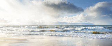 Kumlu sahilden Baltık denizinin panoramik görüntüsü (kum tepeleri). Parlayan bulutları, güneş ışınları olan dramatik bir gökyüzü. Dalgalar, su sıçramaları. Idyllic deniz manzarası. Sıcak kış havası, iklim değişikliği, doğa. Danimarka