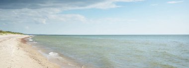 Baltık deniz kıyısı. Açık mavi gökyüzü. Yumuşak güneş ışığı. Kumsal, kum tepeleri, çakıl taşları. Saf doğa, çevre koruma, ekoloji, eko-turizm, yürüyüş, yaz tatili, dinlenme. Panoramik görünüm