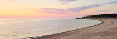 Mavi gökyüzünün altında, parlak pembe ve altın renkli günbatımı bulutlarıyla Baltık deniz kıyısında. Kaya kıyısı, dalgalar. Idyllic deniz manzarası. - Letonya. Doğa, çevre koruma, eko-turizm. Resim gibi bir manzara.