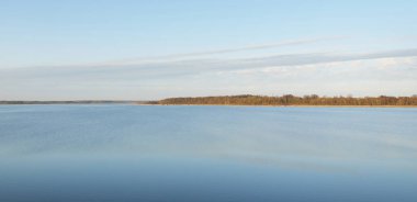 Gün batımında mavi orman gölü (nehir) panoramik hava manzarası. Yumuşak güneş ışığı, berrak gökyüzü, suya yansıyan yansımalar. Baharın başında. İdealist pastoral manzara. Doğa, çevre, ekoloji, eko-turizm