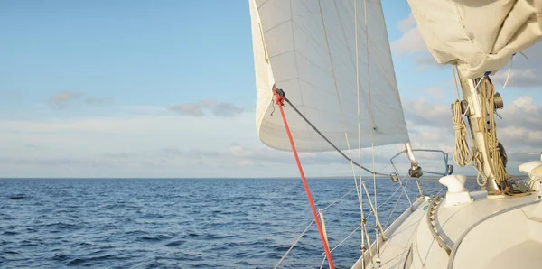 Gün batımında açık denizde yelkenli yelkenli yelkenli. Gökyüzü açık. Güverteden pruvaya bir manzara, direk, yelkenler. Ulaşım, seyahat, gezi, spor, eğlence, boş zaman aktivitesi, yarış, yelkenli yarışı