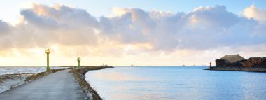 Eski iskele (yürüyüş yolu, gezinti) deniz fenerine. Dalgakıranlar yakın çekim. Açık mavi gökyüzü, pembe günbatımı bulutları, altın güneş ışığı. Deniz manzarası, bulut manzarası. Baltık Denizi. Bahar. Turizm, dönüm noktası, navigasyon
