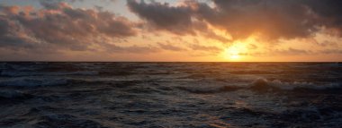 Mavi gökyüzünün altında, parlak pembe ve altın renkli günbatımı bulutlarıyla Baltık deniz kıyısında. Kaya kıyısı, dalgalar. Dalgalar çarpıyor. - Letonya. Doğa, çevre koruma, eko-turizm. Resim gibi bir manzara.