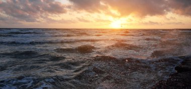 Mavi gökyüzünün altında, parlak pembe ve altın renkli günbatımı bulutlarıyla Baltık deniz kıyısında. Kaya kıyısı, dalgalar. Dalgalar çarpıyor. - Letonya. Doğa, çevre koruma, eko-turizm. Resim gibi bir manzara.