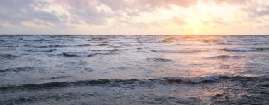 Fırtınadan sonra parlayan günbatımı bulutlarıyla mavi gökyüzünün altında Baltık Denizi kıyısında. Su yüzeyi dokusu, çarpan dalgalar. Doğa, çevre koruma, eko-turizm. Resimli panoramik manzara