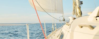 Gün batımında açık denizde yelkenli yelkenli yelkenli. Gökyüzü açık. Güverteden pruvaya bir manzara, direk, yelkenler. Ulaşım, seyahat, gezi, spor, eğlence, boş zaman aktivitesi, yarış, yelkenli yarışı