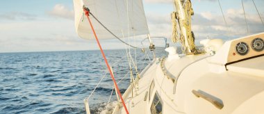 Gün batımında açık denizde yelkenli yelkenli yelkenli. Gökyüzü açık. Güverteden pruvaya bir manzara, direk, yelkenler. Ulaşım, seyahat, gezi, spor, eğlence, boş zaman aktivitesi, yarış, yelkenli yarışı