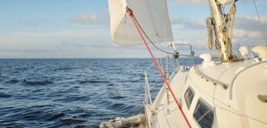 Gün batımında açık denizde yelkenli yelkenli yelkenli. Gökyüzü açık. Güverteden pruvaya bir manzara, direk, yelkenler. Ulaşım, seyahat, gezi, spor, eğlence, boş zaman aktivitesi, yarış, yelkenli yarışı