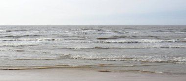 Gün batımında Baltık kıyısı. Yumuşak güneş ışığı, parlayan bulutlar, dalgalar ve su fışkıran berrak gökyüzü. Idyllic deniz manzarası. Hava, iklim değişikliği, doğa