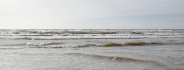 Gün batımında Baltık kıyısı. Yumuşak güneş ışığı, parlayan bulutlar, dalgalar ve su fışkıran berrak gökyüzü. Idyllic deniz manzarası. Hava, iklim değişikliği, doğa
