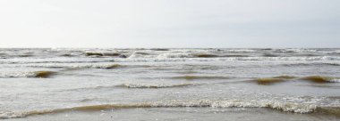 Gün batımında Baltık kıyısı. Yumuşak güneş ışığı, parlayan bulutlar, dalgalar ve su fışkıran berrak gökyüzü. Idyllic deniz manzarası. Hava, iklim değişikliği, doğa