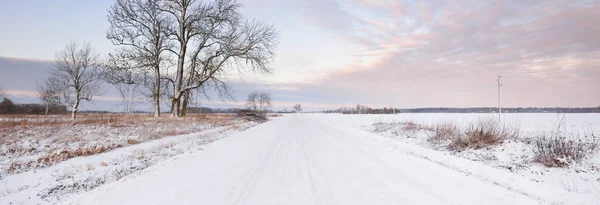 雪のフィールドを介して農村部の道路覆われた 送電線 変圧器の棒 車からのパノラマビュー カラフルな雲 劇的な夕日の空 オフロード 冬のタイヤ リモート村 — ストック写真