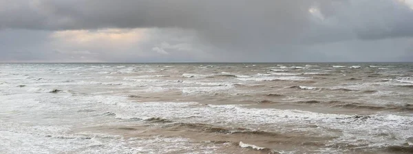 Baltic sea after the storm. Dramatic sky, glowing clouds, soft sunlight. Waves, splashing water. Picturesque scenery, seascape, nature. Panoramic view