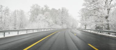 Karla kaplı ormanda boş otoyol (asfalt yol). Kanada mı? Doğa, Noel tatilleri, uzak yerler, kış lastikleri, tehlikeli sürüş konsepti