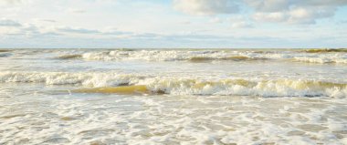 Kumlu bir sahilden (kum tepeleri) Baltık denizinin panoramik görüntüsü. Parlayan bulutlarla, dalgalarla ve su sıçramalarıyla berrak bir gökyüzü. Idyllic deniz manzarası. Sıcak kış havası, iklim değişikliği, doğa