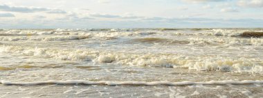 Kumlu bir sahilden (kum tepeleri) Baltık denizinin panoramik görüntüsü. Parlayan bulutlarla, dalgalarla ve su sıçramalarıyla berrak bir gökyüzü. Idyllic deniz manzarası. Sıcak kış havası, iklim değişikliği, doğa